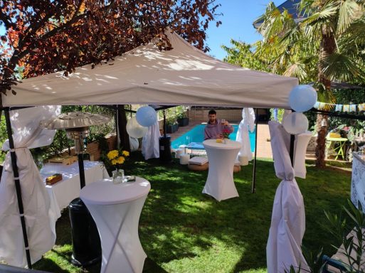 Carpa de jardín decorada para un evento, con mesas y piscina al fondo.